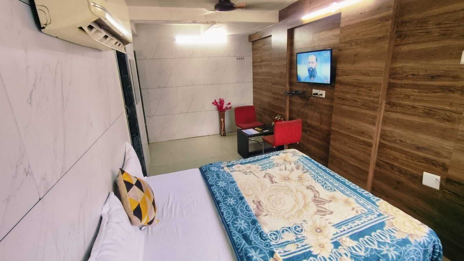 Una habitación de hotel con una cama, un televisor montado en la pared, una silla roja y una mesita.