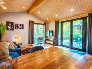 A modern living room with a wooden ceiling, a television, a sofa, a dining table, and large sliding glass doors leading to an outdoor area. - Holiday Home for Four in Ruinen (Ruinen)