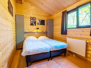 A wooden cabin bedroom with a bed, a radiator, and a window. - Holiday Home for Four in Ruinen (Ruinen)