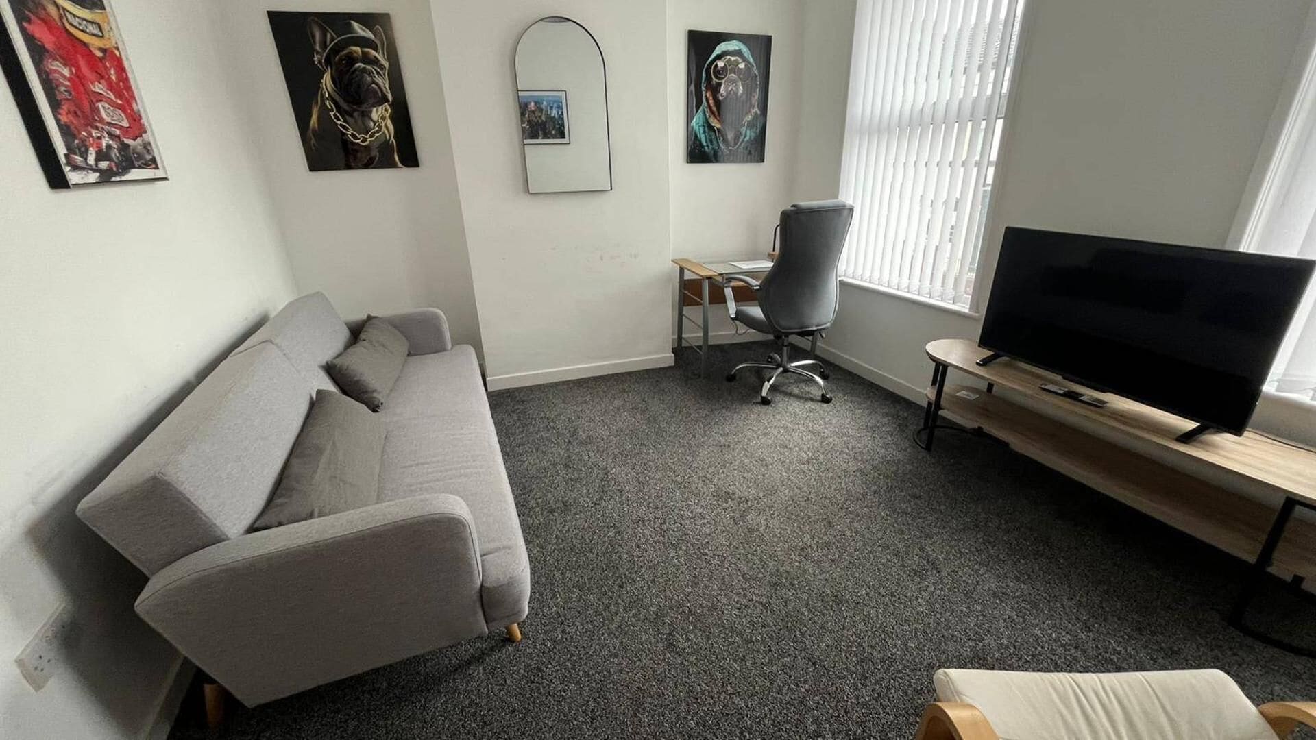 A living room with a grey sofa, a TV on a wooden stand, and artwork on the walls.