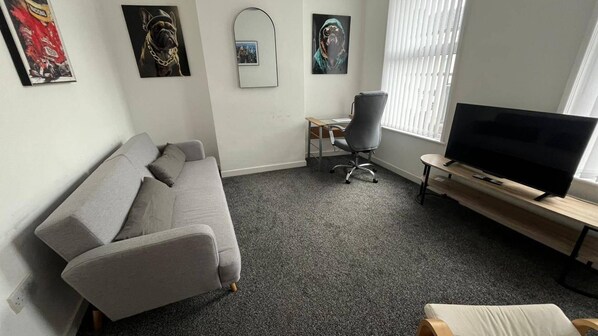 A living room with a grey sofa, a TV on a wooden stand, and artwork on the walls.