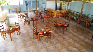 A dining area with multiple wooden tables and chairs, a bar area, and a seating area with a sofa. - Bustani Oasis with AC,Pool, Family-Friendly, Couples, Beach 5 Min Walk (Nungwi)