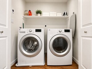 A laundry room with two white LG front-loading washing machines, a shelf above with cleaning supplies, and a towel rack.