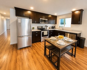 A modern kitchen with dark cabinetry, stainless steel appliances, and a wooden dining table set for four.