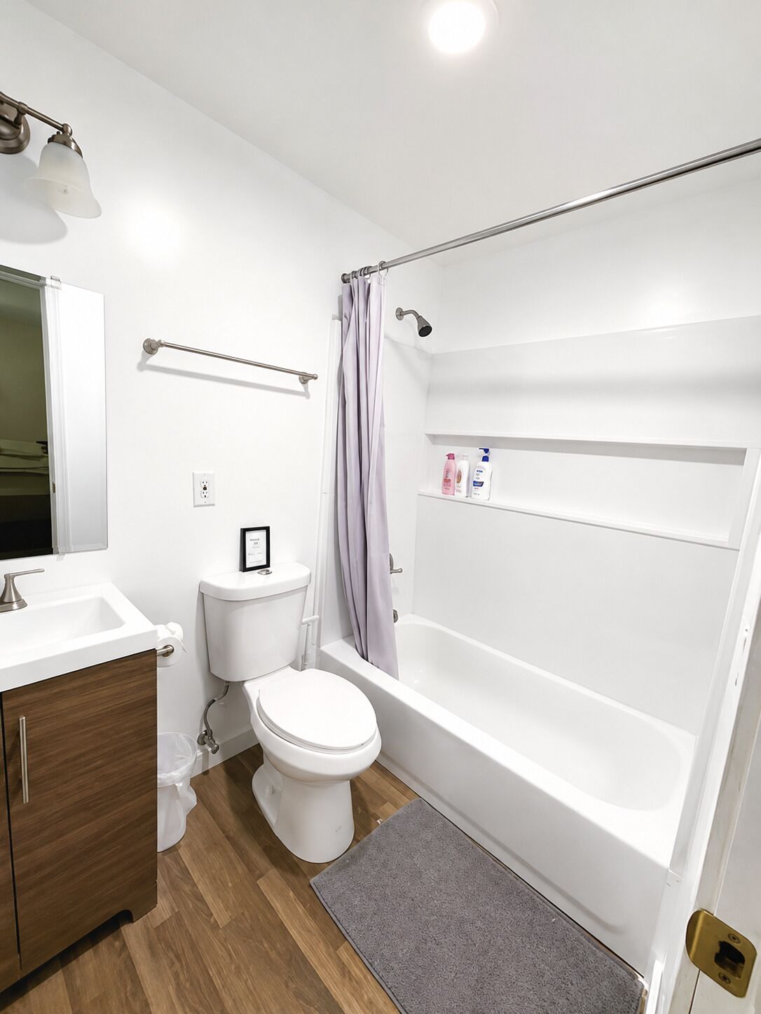 Een moderne badkamer met een wit wastafel, toilet en bad. Boven het toilet bevindt zich een handdoekhouder en er is een douchegordijn.