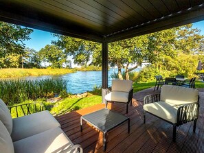 An outdoor patio with a view of a lake, surrounded by greenery and furnished with seating. - Modern Waterfront Villa Retreat for 4 (Wanneperveen)