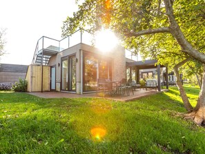 A modern house with a patio, a wooden deck, and a glass door leading to the interior. - Modern Waterfront Villa Retreat for 4 (Wanneperveen)