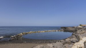 A coastal landscape with a rocky shoreline, a small circular water feature, and a building with a sloped roof. - CHL Casa El Remo mar y Tranquilidad en La Palma (Los Llanos de Aridane)