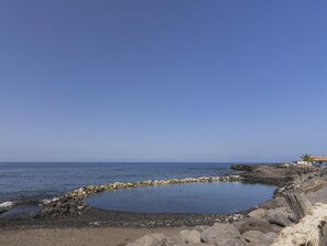 A coastal landscape with a rocky shoreline, a small circular water feature, and a building with a sloped roof. - CHL Casa El Remo mar y Tranquilidad en La Palma (Los Llanos de Aridane)