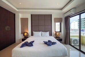 A hotel room with a large bed, two bedside tables, a headboard, and a view of buildings through the window. - President Park Patong (Patong)