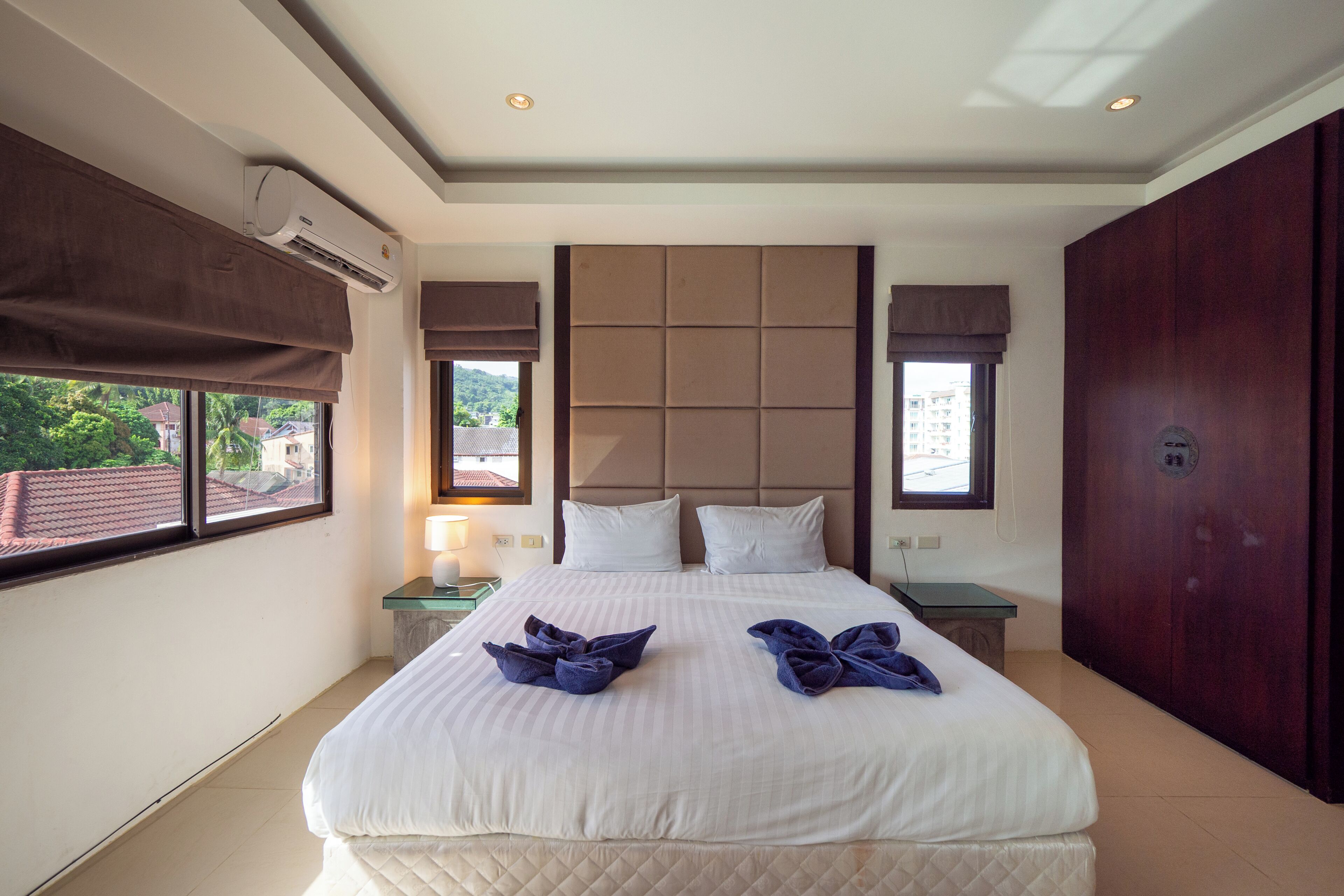 A hotel room with a large bed, a nightstand, an air conditioning unit, and a view of the outside.