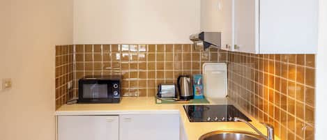 A compact kitchen with white cabinets, a microwave, a toaster, a kettle, and a sink.