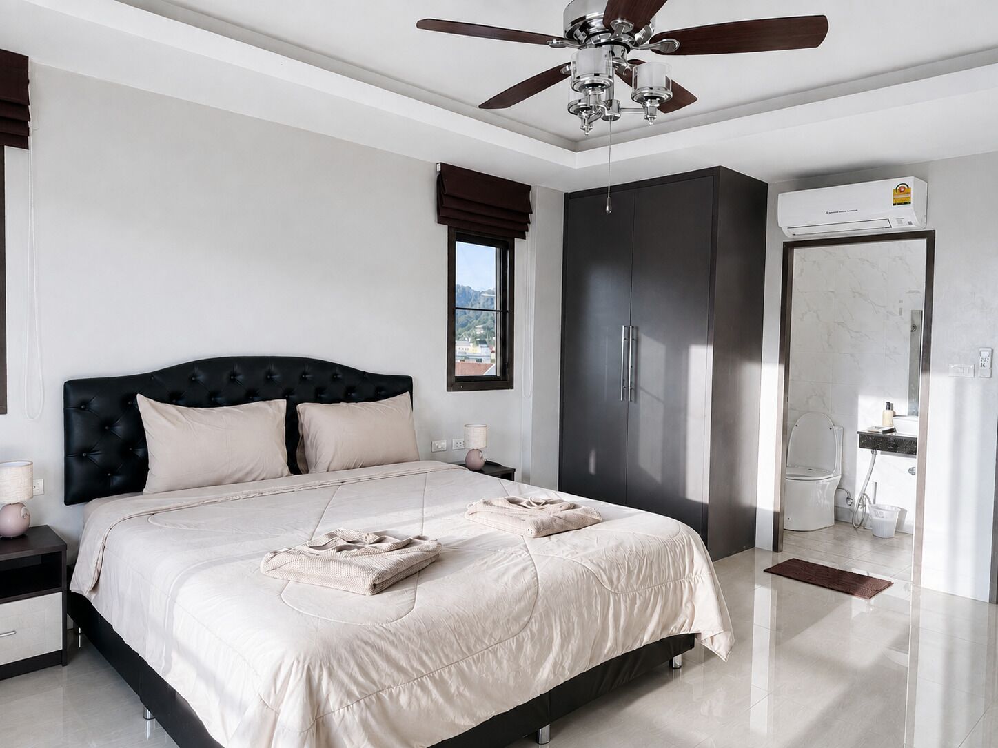 Un dormitorio con cama, ventilador de techo, armario y baño con inodoro y lavamanos.