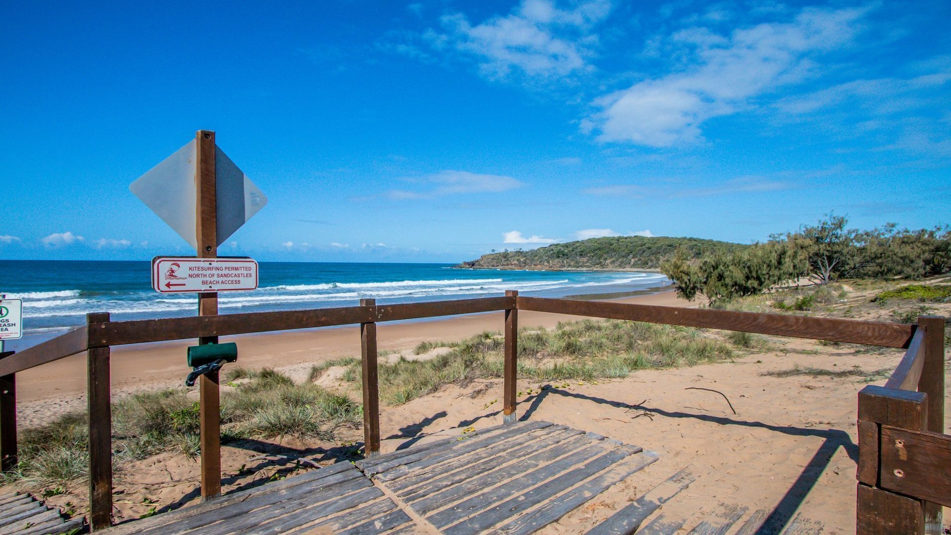 A wooden boardwalk leading to a beach with a sign indicating kitesurfing permitted north of Sandcastles Beach Access.