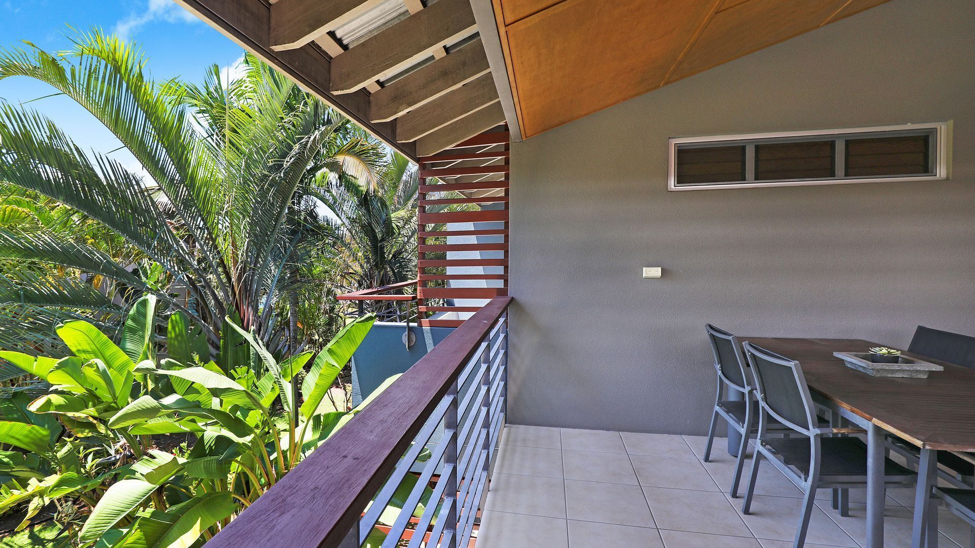 A balcony with a wooden railing, a table with chairs, and tropical plants.