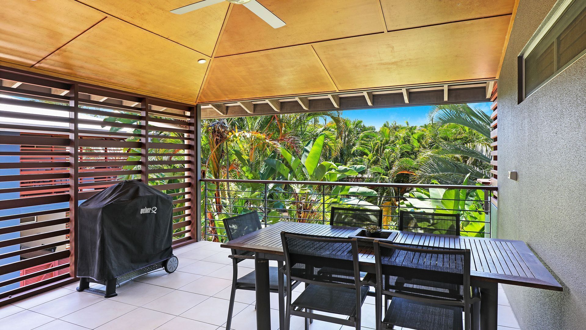 Un balcon avec une table et des chaises, un barbecue et une vue sur une végétation luxuriante.