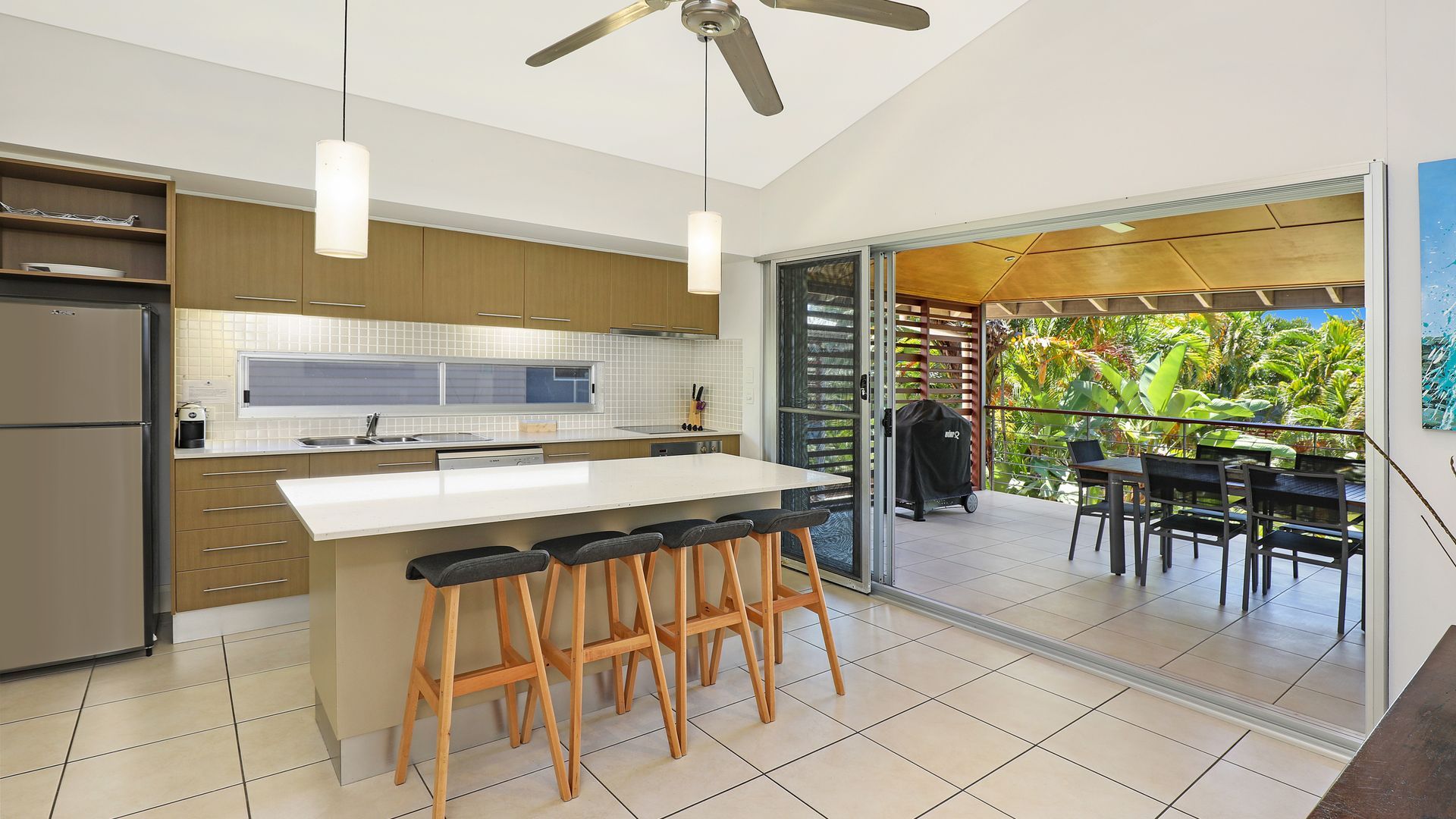 A modern kitchen with a central island, bar stools, and a view of an outdoor dining area.