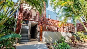 A modern building with a staircase leading to a covered entrance, surrounded by lush tropical plants. - Tide n Town - 2 bedroom resort apartment - pools, restaurant (Agnes Water)