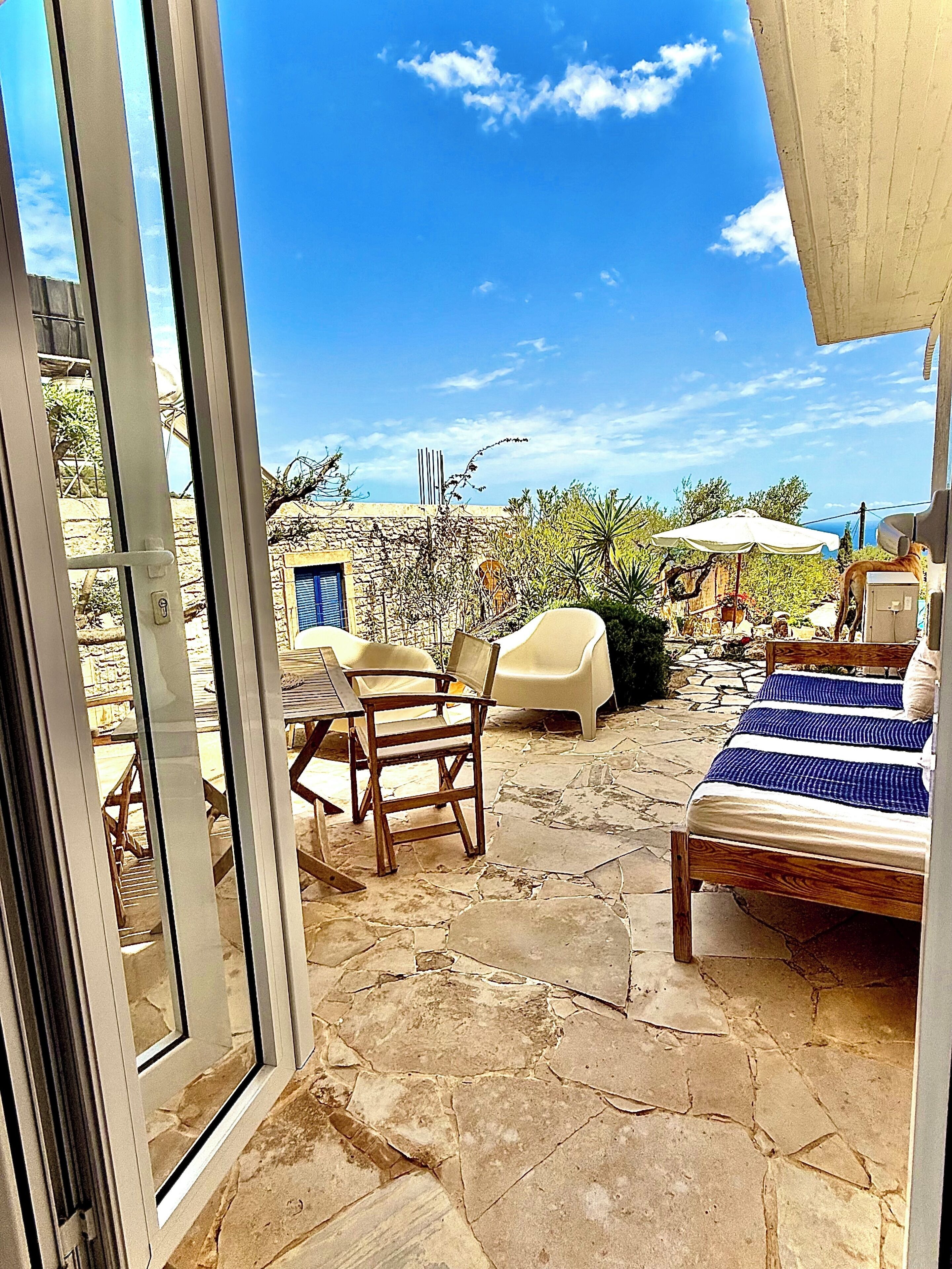 An outdoor patio with stone flooring, a bed, and two chairs.