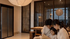 A modern living room with a wooden coffee table, a large hanging light fixture, and a sliding door. - Hanwo House PIK (Jakarta)