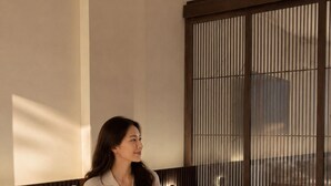 A person sitting on a bed with a tray of breakfast items, including fruits, croissants, and juice. - Hanwo House PIK (Jakarta)
