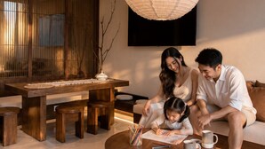 A modern living room with a round coffee table, a dining area with a wooden table and benches, and a large hanging light fixture. - Hanwo House PIK (Jakarta)
