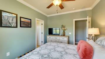 A bedroom with a bed, a ceiling fan, a television, a dresser, and two framed pictures on the wall.