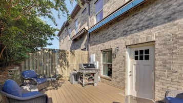A deck with outdoor furniture, a barbecue grill, and a brick building with a white door.