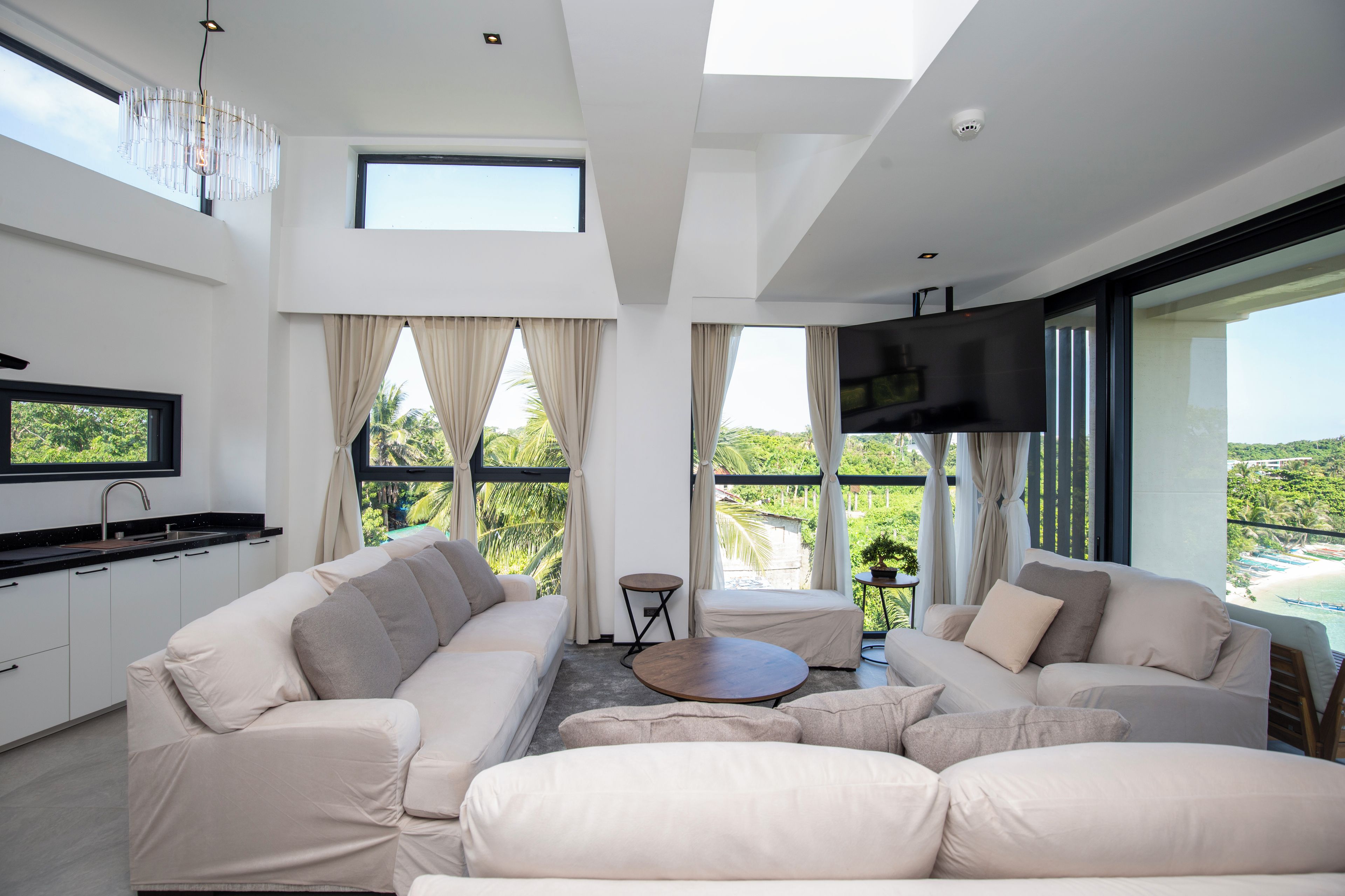 A modern living room with a sofa set, a television, and a kitchen area with a sink.