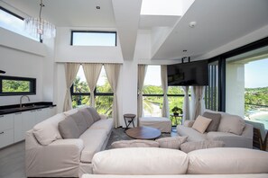 Una sala de estar moderna con un conjunto de sofás, una televisión y una cocina con pileta.