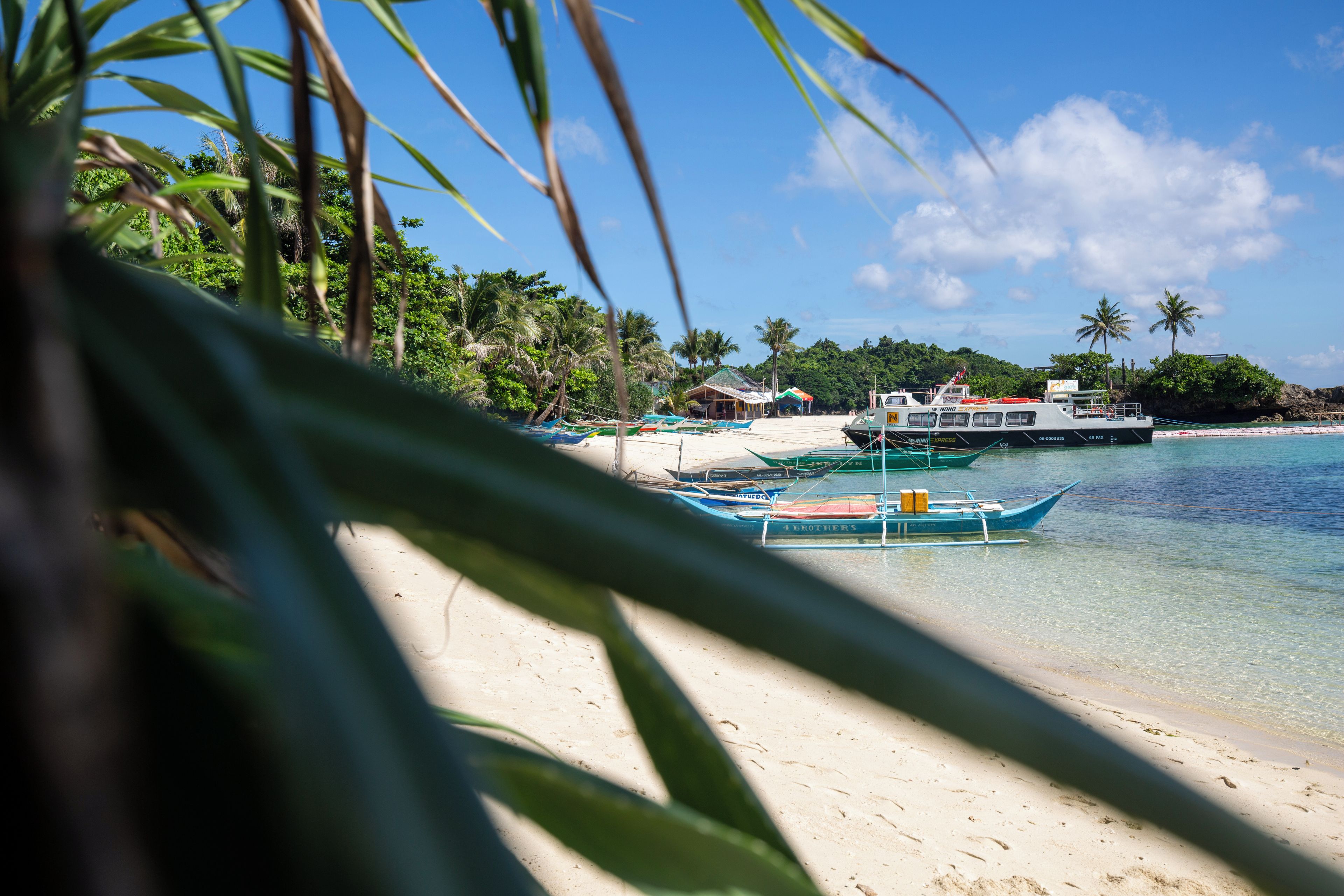 A beach with clear water, boats, and palm trees.