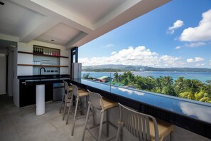 A modern kitchen with a bar area, a dining space with chairs, and a large window offering a view of a coastal landscape. - Paradise Ocean View Boracay (Malay)