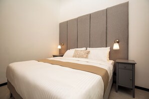 Una habitación de hotel con una cama grande, dos mesitas de noche y un cabecero.
