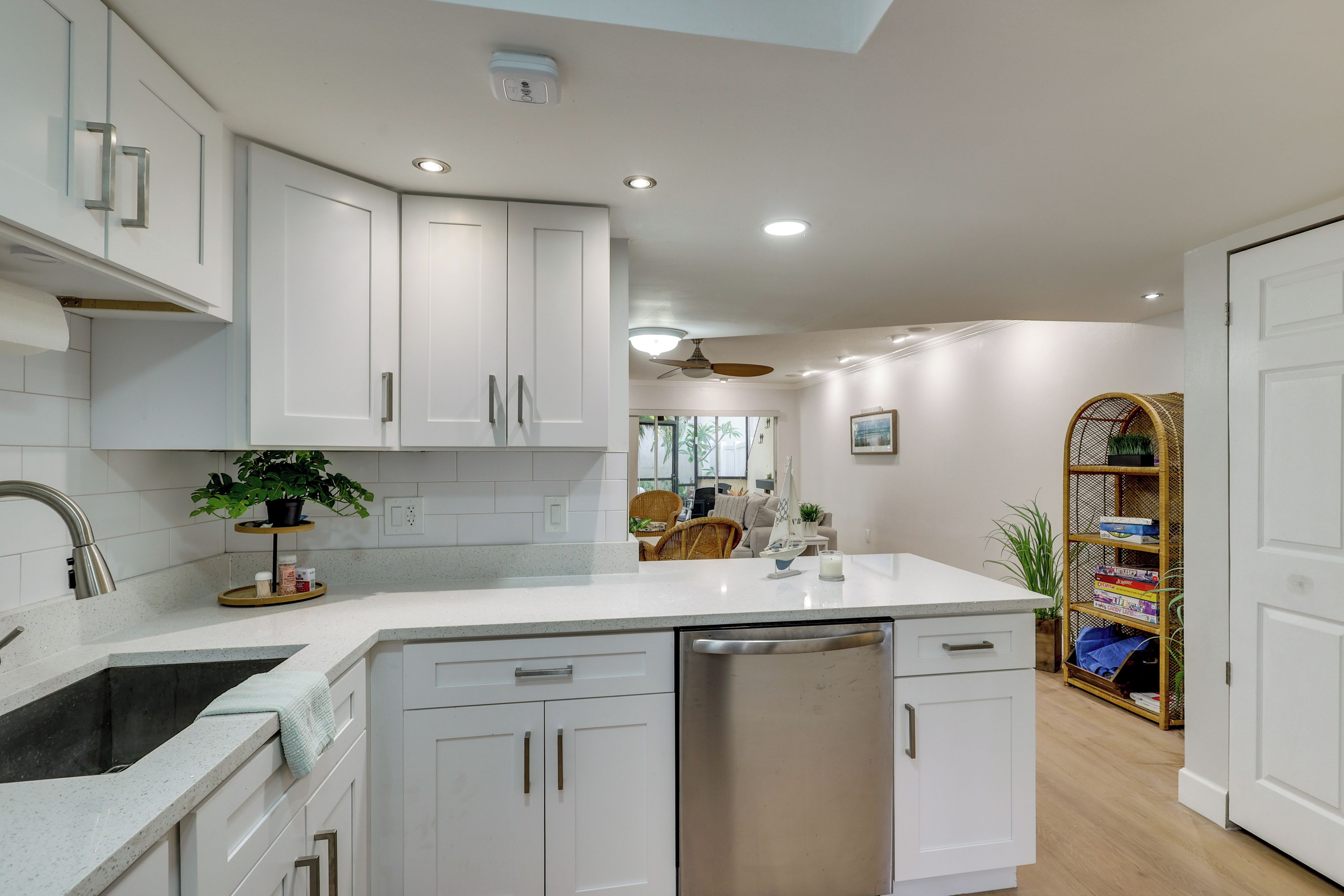 A modern kitchen with white cabinetry, a dishwasher, and a countertop with a plant.