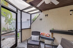 Ein überdachter Patio-Bereich mit Korbmöbeln, einem Deckenventilator und Blick auf einen Garten.