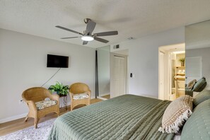 Un dormitorio con una cama, dos sillas de mimbre, un televisor, un ventilador de techo y un armario.