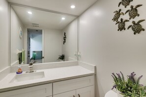 Un baño con un espejo grande, un mostrador blanco y detalles decorativos de tortugas en la pared.