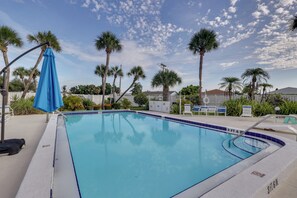 Una piscina con lona azul, palmeras y una valla blanca.