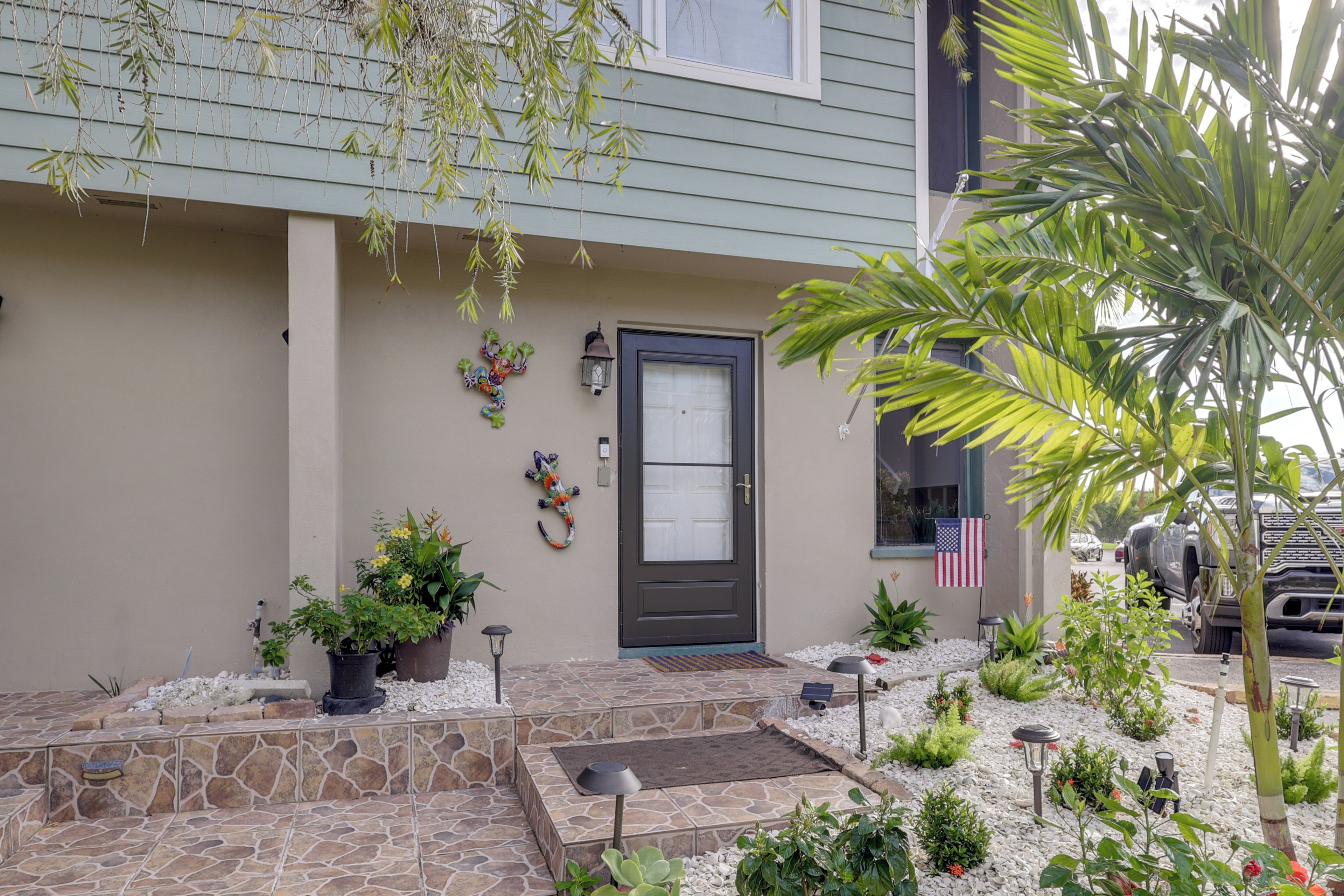 A house with a front porch, a door, and a small garden with plants and a flag.