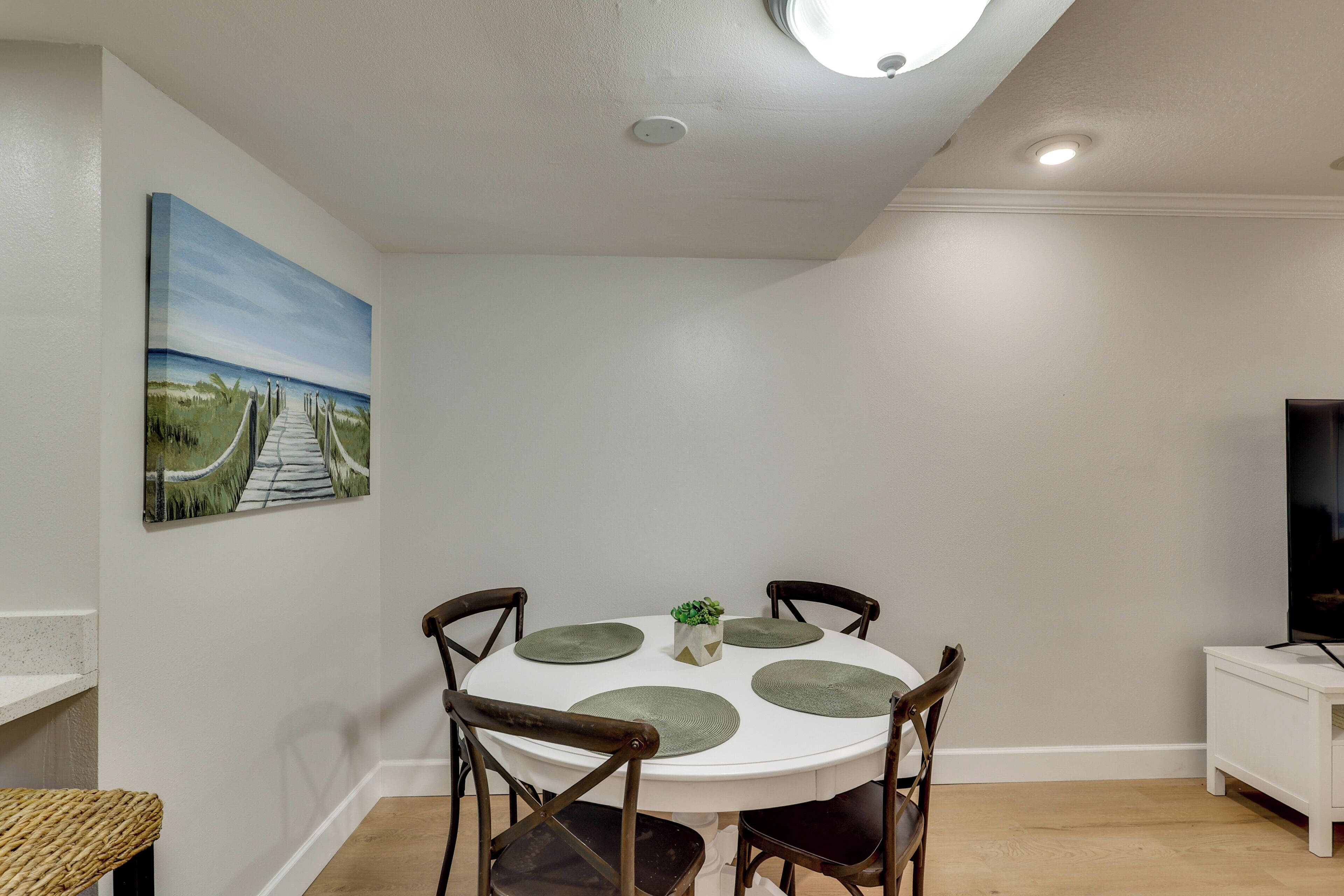 A dining area with a round table, four chairs, a small plant, and a painting on the wall.