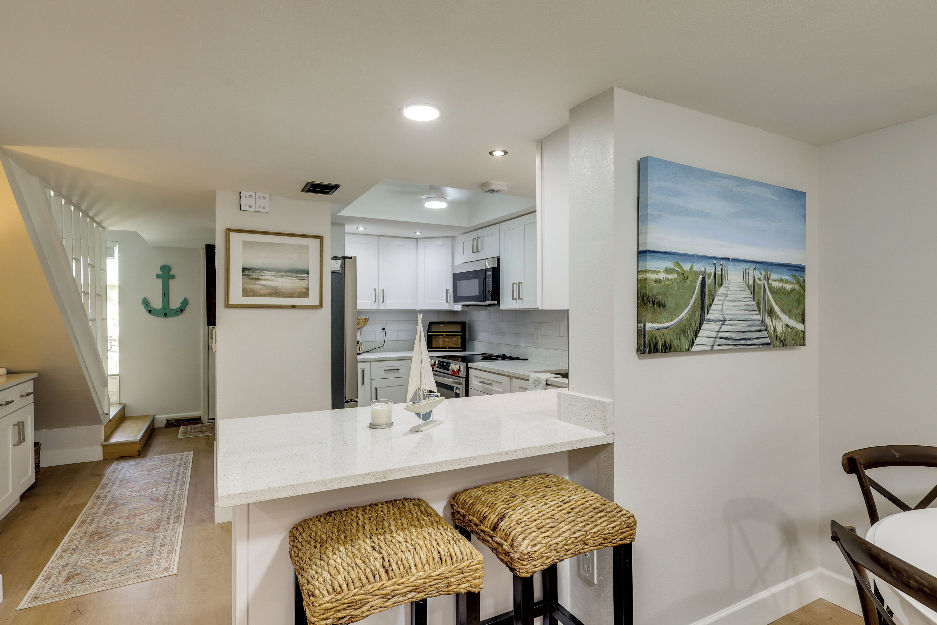 A modern kitchen with white cabinets, a microwave, and a small island with stools.