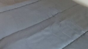 A bed with grey bedding and two pillows, one yellow and one grey.
