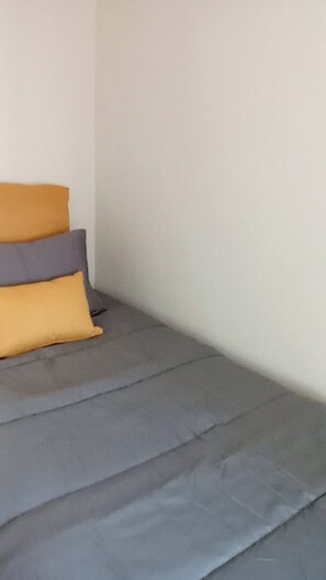 A bed with grey bedding and two pillows, one yellow and one grey.