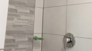 A bathroom with a shower area featuring a tiled wall and a corner showerhead.