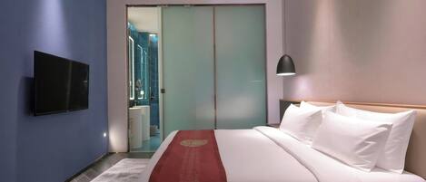 A hotel room with a bed, a TV mounted on the wall, a bedside lamp, and a view of the bathroom through a sliding door.