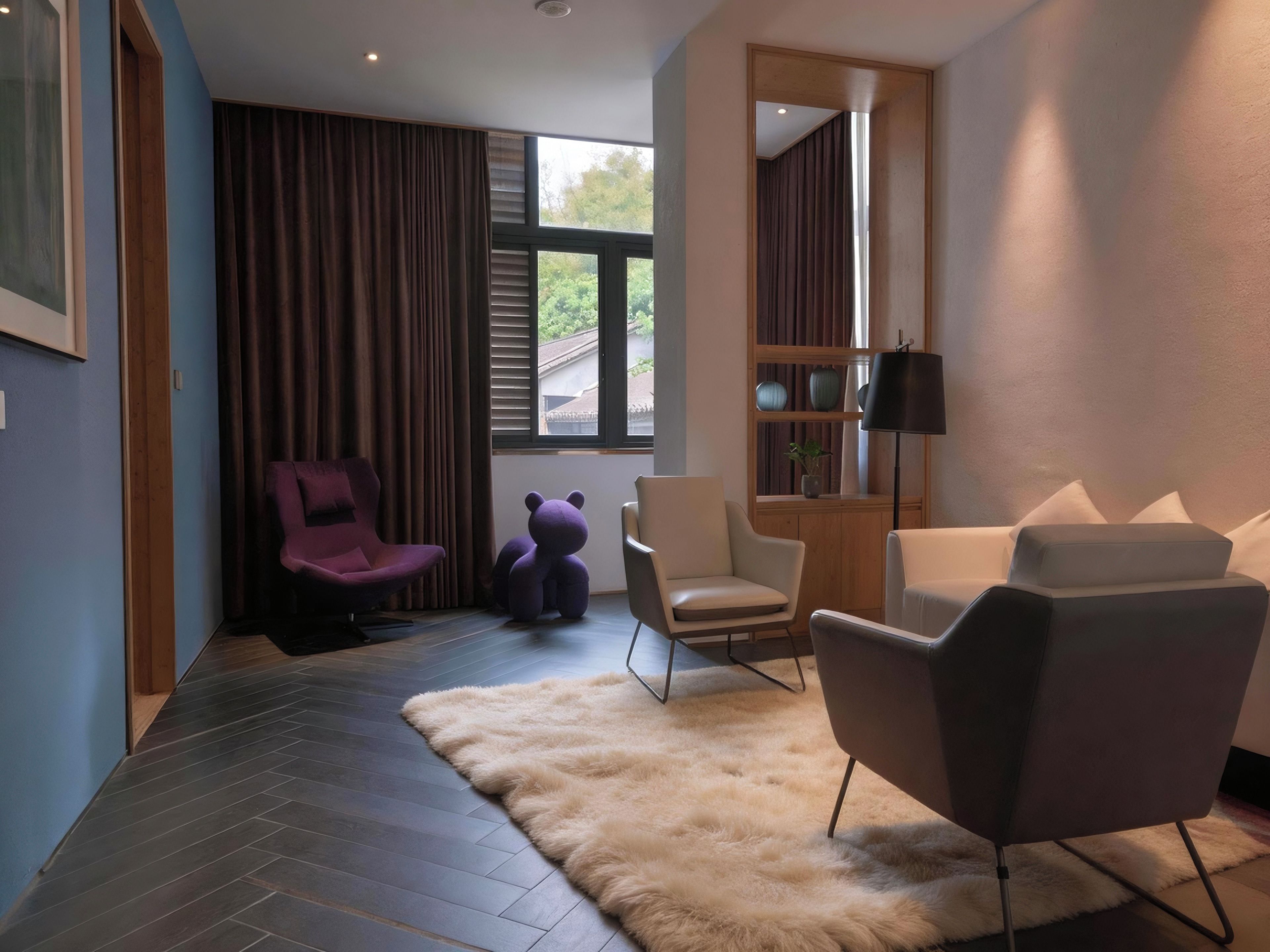 A modern living room with a sofa, chairs, a rug, and a bookshelf.