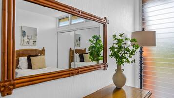 A room with a bed, a mirror, a vase with a plant, and a lamp.