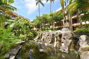 A hotel courtyard with a water feature, palm trees, and lush greenery. - Beachfront 2BD w Stunning Ocean View-paki Maui 424 (Kaanapali)