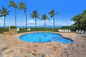 A swimming pool with a stone deck, surrounded by palm trees and lounge chairs, with a view of the ocean. - Beachfront 1BD w Stunning Ocean View-paki Maui 207 (Kaanapali)