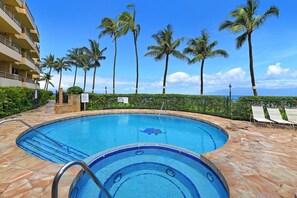 A swimming pool with a stone deck, surrounded by palm trees and a building with balconies. - Beachfront 1BD w Stunning Ocean View-paki Maui 207 (Kaanapali)